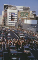 Shinjuku. Crowded pedestrian crossing on busy city road with queues of traffic waiting to proceed