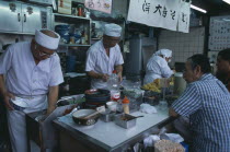 Tsukiji Fish Market. Chefs working in the open kitchen of a food bar with customers sitting at the counter