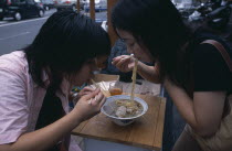 Tsukiji Fish Market. Two girls sharing a bowl of noodles at a street stall