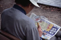 View over the shoulder of a man reading the newspaper with a magnifying glass