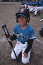 Young boy kneeling on the grass wearing a Baseball kit holding a bat