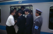 Passengers crowding on to a train at Ueno Station with train guard standing on the platform