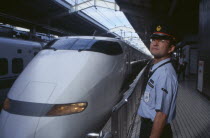 Bullet train aka Shinkansen pulling into the station platform with train guard standing in the foreground