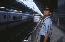 Bullet train aka Shinkansen pulling into the station platform with train guard standing in the foreground