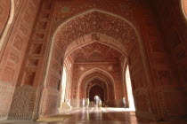 Taj Mahal  with an 9nterior view of the elaborate red sandstone hallway and arches of the western mosque with people walking through