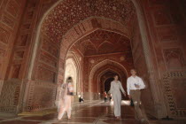 Taj Mahal  with an 9nterior view of the elaborate red sandstone hallway and arches of the western mosque with people walking through