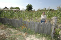 Elderly female farmer standing in corn field behind wooden fence
