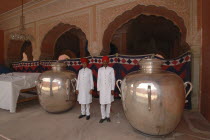 At the Jaipur city palace two guards dressed in white with red turbans standing between two massive silver urns used by the Maharaja Sawai Mansingh II to carry holy water from the Ganges
