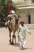 Man leading camel with three children riding on its back