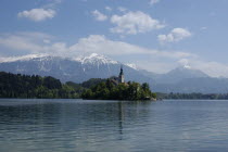 View over the lake toward Bled Island and tower of the Church of the Assumption with snow capped peaks of the Julian Alps behind
