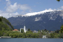 Pristiva. View from the lake toward the Church of St Martin with snow capped peaks behind