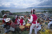 Group of Bai ethnic minority girls in traditonal costume above a market with the sea in the distance.
