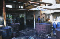Weishan. Batik factory with men working around  vats of dye under ornings.