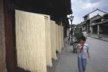 Weishan. Racks of noodles hanging out to dry in street with a boy walking past on pavement.