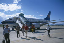 Domestic aircraft on runway with passengers disembarking.