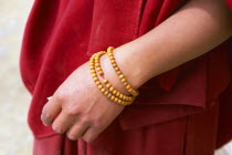 Tibet, Shigatse, Detail of a monks hand with a rosary wrapped around his wrist wearing a red robe.