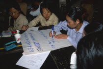 China, Yunnan Province, Simao. Pu er. Teachers sat around a table preparing a presentation on flip chat paper at a training workshop for teachers.