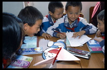 China, Yunnan Province, Children in their classroom working in groups with various school materials on the table in front of them.
