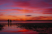 Two figures silhouetted on the beach watching a dramatic sunset