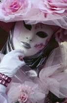 Venice Carnevale. Close up portrait of a female figure dressed in a white and pink floral costume and mask