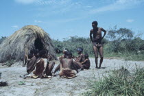 Bushmen gathered next to straw hut.