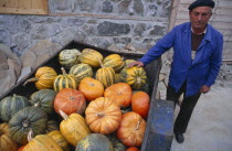 Pumpkin farmer standing beside his crop in a cart beside him