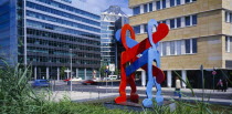Red and blue sculpture by Keith Haring entitled Boxers with city road and architecture behind