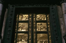Close up of black wooden Baptistry door of the Duomo with pannels of carved gold depicting stories from the Old Testament