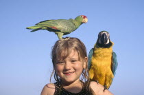 Portrait of a young girl with yellow and blue Parrot on her shoulder and a green and red Paroquet on her head