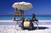 Beach vendors stall on a bicycle selling musical instruments and hats with clear blue sea beyond