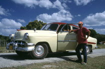 Man standing by the open door of a classic style American car which has been fitted with tractor tyres due to a tyre shortage
