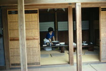 Home of the potter Chinjukau with moveable wooden screens open to reveal interior with woman laying table.