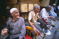 Group of men smoking sheesha water pipes and drinking tea in an ahwa or coffee house.