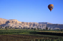 Valley of the Kings with hot air balloon above agricultural land  village and limestone hills with distant tombs.