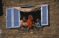 City housing with women at open window with blue and white wooden shutters.