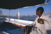 Cropped view of man on board felucca looking across water towards others.