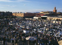 Djemma El Fina. View over busy market square lots of people around stalls with buildings behind.