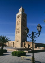 Koutoubia Mosque. Tower seen from pavement with blue sky behind. palm trees in front.