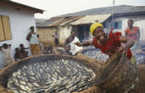 Laughing woman smoking fish over mud brick ovens