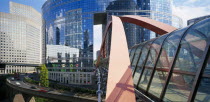 La Defense.  Covered pedestrian bridge over busy road with circular  glass fronted building reflecting city skyline behind.