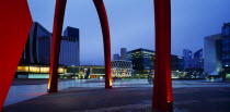 La Defense.  Alexander Calders red iron stabile sculpture.  Part view with city buildings behind illuminated at night.