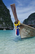 Maya Bay.  Close view of prow of long tail boat draped with flower garlands.  Limestone rocks behind.