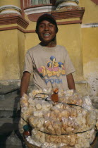 Street food vendor with basket piled with bags of popcorn and other snacks.