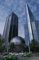 Financial district in Zona Rosa on Paseo de La Reforma.  Domed roof of bank surrounded by high rise buildings  green volkswagon taxis on road in the foreground.