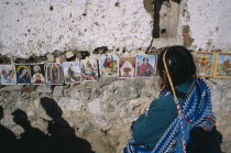 Woman in front of coloured pictures of the lives of the Saints and Christ displayed along stone wall.