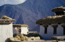 Farmer winnowing barley by mountain village farm buildings