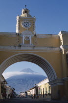 Arco de Santa Catarina. Yellow painted archway with clock tower and people walking  with Volcan Agua visible through arch.Volcano