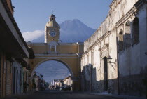 Arco de Santa Catarina. Yellow painted archway with clock tower and people walking underneath  with Volcan Agua beyond.Volcano