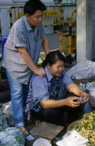 Wholesale Food Market.  Female vendor seated at vegetable stall having her shoulders massaged.