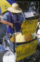 Khao San Road. Pad Thai food street stall with price signs and man preparing food behind counter.